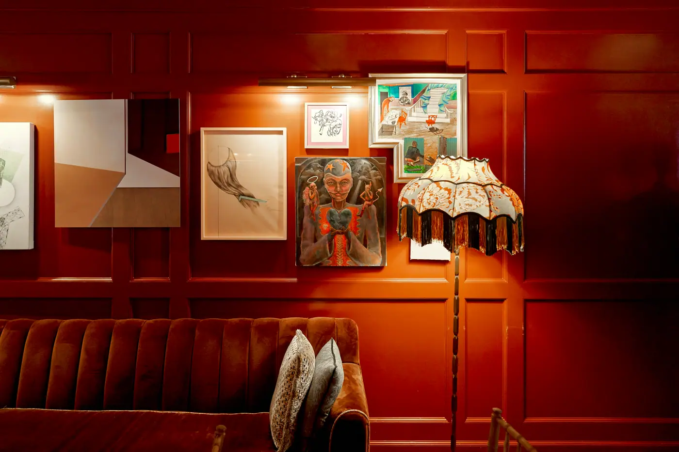 The Ned NoMad's maroon gallery wall with paintings, a velvet sofa and a fringed lamp